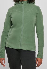 Giacca in fleece verde con zip frontale, cappuccio e due tasche laterali. Presenta una texture liscia e un design aderente.