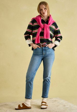 Gestreiftes langärmeliges Hemd in Grün, Pink und Weiß, überlagert mit einem pinken Pullover. Blaue Jeans und braune Sandalen mit weißen Socken runden den Look ab.