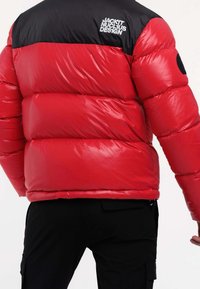 Red and black puffer jacket with "Jack It Nuclius Design" logo on upper back, worn with black pants, shown from behind and side.