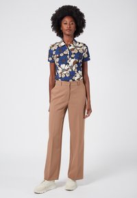 Bloemenpatroon shirt in blauw, crème en bruin met een kraag. Beige high-waisted broek. Witte sneakers met gestructureerde zolen.