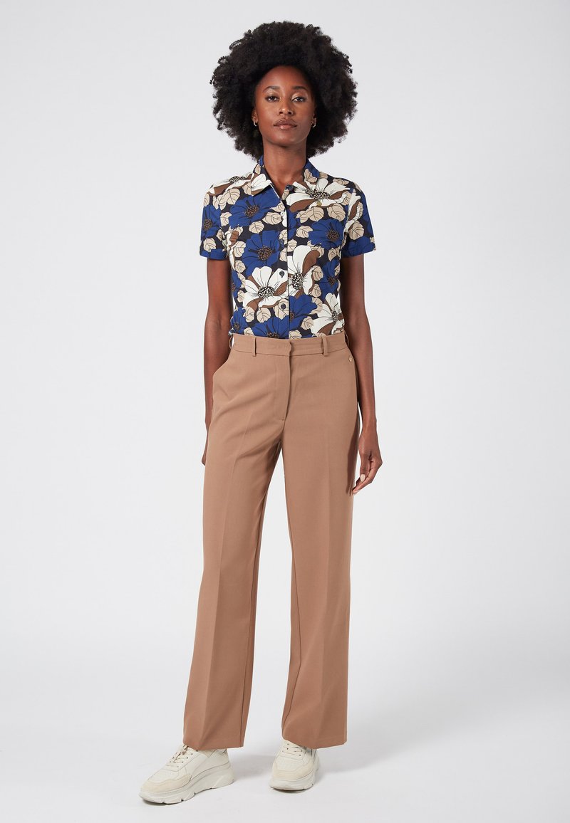 Bloemenpatroon shirt in blauw, crème en bruin met een kraag. Beige high-waisted broek. Witte sneakers met gestructureerde zolen.