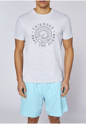 Man wearing light gray T-shirt with ocean wave and sun graphic and text, paired with light blue shorts with matching logo.