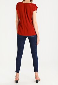 Kraprød kortærmet top med en afslappet pasform, kombineret med mørkeblå skinny jeans. Toppen har diskrete samling detaljer på skuldrene.
