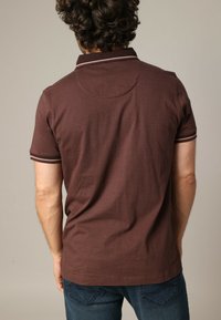 Polo shirt marron à manches courtes avec un col et des rayures de manches contrastants, fabriqué en tissu texturé. Il présente un ourlet droit et un motif discret.