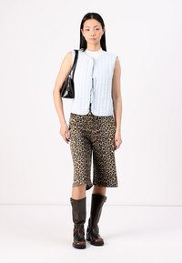 Svetlomodrá prešívaná vesta bez rukávov, biela blúzka pod ňou, leopardí vzorované culottes a hnedé vysoké čižmy po kolená. Čierna kabelka dopĺňa outfit.