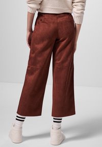 Bruna faux suede vida byxor med bakfickor, med en slät textur. Stylad med vita sneakers och svartspräckta strumpor.