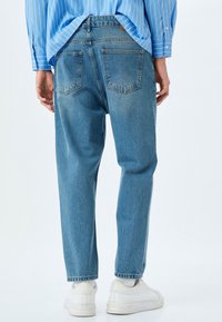 Vaqueros de mezclilla de color azul claro con corte relajado, con dos bolsillos traseros, ligero desgaste, y combinados con zapatillas blancas.