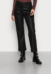 Pantalons en simili cuir noirs à taille haute, avec une coupe droite, texture lisse, et associés à des bottines noires avec détail de boucle.