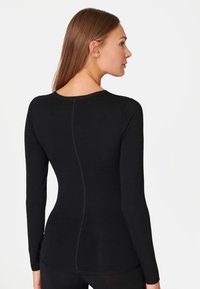 Zwarte langslijfige top met een ronde halslijn en een getailleerde silhouet. Gemaakt van zachte stof, met een centrale naaddetail aan de achterkant.
