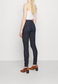 Höga mörka denimjeans med smal passform, med en design för bakfickor. Matchas med bruna högklackade skor och en vit linne.