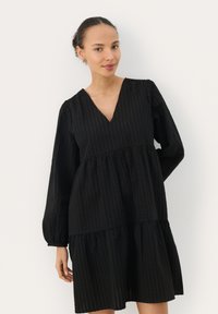 Robe noire avec un décolleté en V, des manches bouffantes longues et des volants en couches. Tissu texturé avec des motifs subtils qui ajoutent de la profondeur au design.