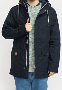 Marinblå jacka i kraftigt tyg, med huva, dragsko, två frontfickor och accenter i beige läder. Dragkedjestängning med tryckknappar.