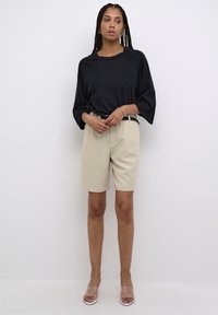 Top negro de gran tamaño con mangas hasta el codo, combinado con pantalones cortos beige hasta la rodilla, un cinturón negro y sandalias de tacón transparentes.