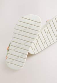 Semelles de sandales en caoutchouc blanc avec motif de grip texturé et taille embossée "12". Accents en tissu floral visibles sur les bords. Fabriqué en Chine.