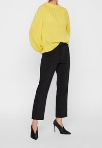 Yellow knitted sweater with a ribbed neckline, oversized sleeves, paired with black slim-fit pants and pointed black heels.