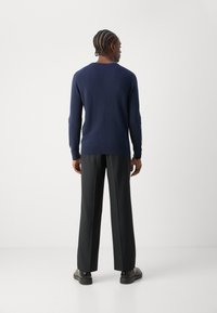 Pull en laine bleu marine avec un col rond, associé à un pantalon noir à jambes larges et des chaussures noires, vu de l'arrière. Texture lisse.