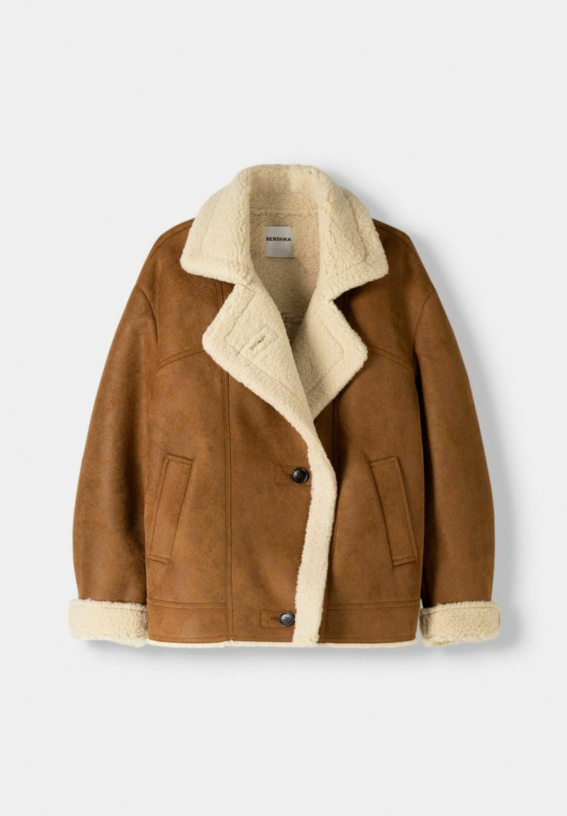 Chaqueta de piel sintética marrón con cuello y forro de borrego crema, que presenta dos bolsillos frontales y un cierre de botón negro.