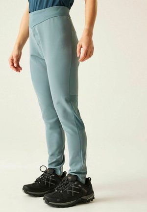 Person wearing light blue fitted pants and black hiking shoes standing on a plain light background.