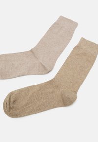 Ein Paar Socken in hellbeigen und dunkleren Khaki-Tönen. Weicher, gestrickter Stoff mit gerippten Bündchen sowie verstärkten Zehen- und Fersenbereichen.