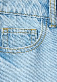 Tissu en denim bleu clair en gros plan montrant une petite poche arrière avec une couture jaune et une partie d'une passants de ceinture sur un jean.