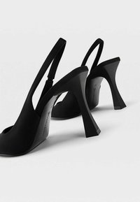 Svarta slingbackklackar med öppen tå, strukturerad tygovandel och geometrisk hög klackdesign. Slät textur och minimalistisk stil.