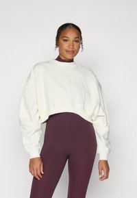 Kappet hvit genser med lange ermer, myk tekstur og ribbede mansjetter, parret med tettsittende burgunder tights. Enkel, ren design.