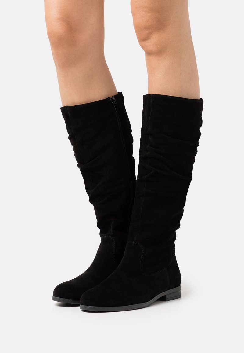 Bottes hautes jusqu'au genou en daim noir avec un design affaissé, fermeture éclair latérale, semelle plate et détails de couture minimalistes. Texture lisse et profil élancé.