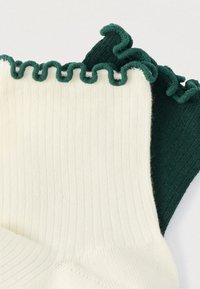 Ριμπ κάλτσες σε κρεμ χρώμα με πράσινη κυματιστή ριγέ άκρη και σκούρο πράσινο τμήμα· μαλακή υφή, με εναλλασσόμενα χρώματα και σχέδιο.