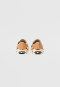 Brune kanvas lave sneakers med rund tå, kontrast hvit gummisåle og svart merkevare på hælen. Enkelt design og flate lisser.