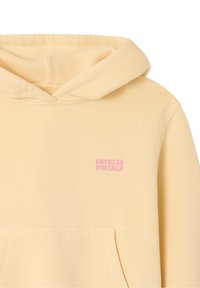 Sweat à capuche jaune pâle avec poche avant et petit texte rose "AMERICAN VINTAGE" sur le côté gauche de la poitrine.