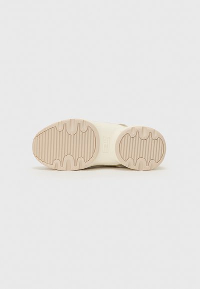 Suela de zapato en crema con ranuras texturizadas para tracción, con extremos redondeados y logotipo. Parte superior no visible.