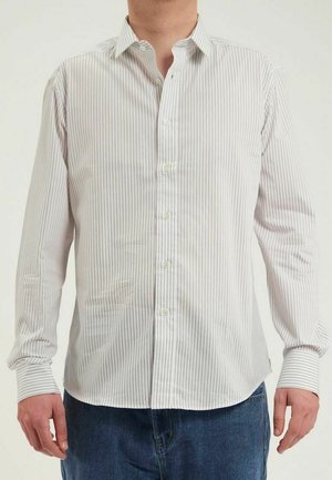 Chemise blanche à manches longues et à boutons, avec des rayures verticales fines et un col évasé. Le tissu semble lisse, avec des poignets boutonnés et une fermeture devant.