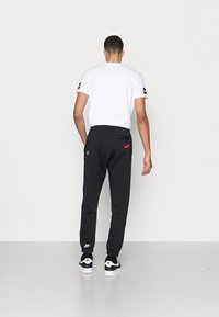 Svarta mjukisbyxor med elastisk midjeband och avsmalnande ben, med röda och blå Nike-logotyper. Bärs med en vit t-shirt och svarta sneakers.