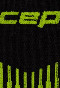 Schwarze Stricksocke mit auffälligem grünen "CEP"-Logo und vertikalen grünen Akzenten. Das Material wirkt weich mit einer strukturierten Oberfläche.