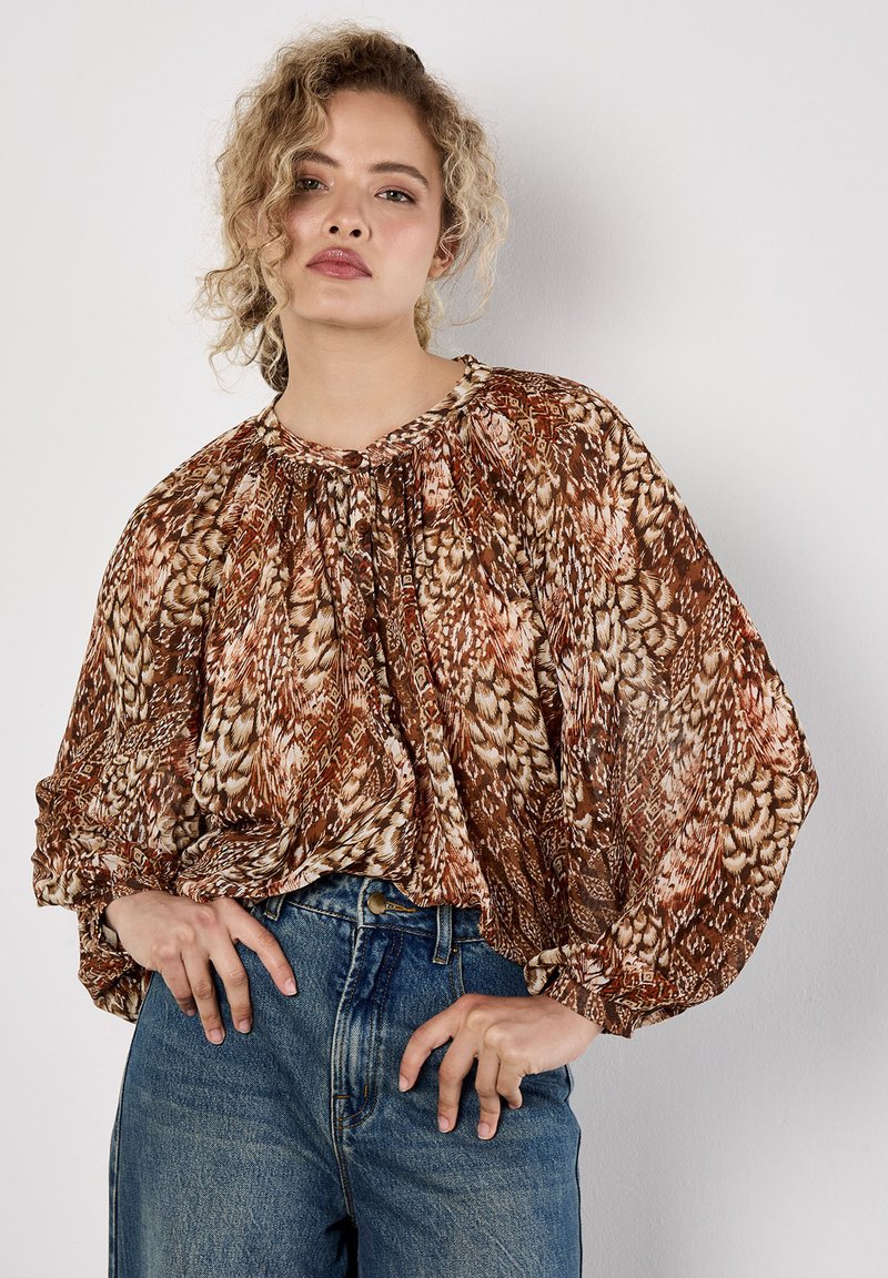 Langärmlige, braun gemusterte Bluse mit gerafftem Ausschnitt und voluminösen Ärmeln, kombiniert mit hoch-taillierten blauen Denim-Jeans.