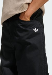 Čierne športové nohavice z hladkej látky s bočnými vreckami a malým bielym logom Adidas na ľavom boku.