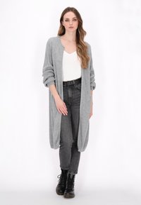 Cardigan lung gri deschis cu deschidere frontală, textură izibilă, și mâneci răsfoite, purtat cu un top alb, jeans închiși la culoare și cizme negre.