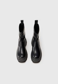 Botines negros de cuero suave, con suela de goma, paneles laterales elásticos y tiradores para facilitar su uso.