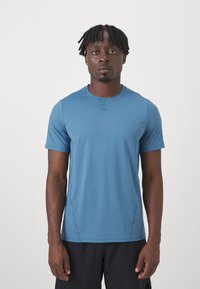 Βαμβακερό κοντομάνικο αθλητικό μπλουζάκι σε μπλε απόχρωση, με ελαφρύ, λείο ύφασμα, στρογγυλή λαιμόκοψη και διακριτές λεπτομέρειες ραφής στα πλάγια.