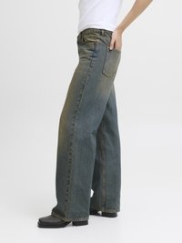 Jeans de denim azul de perna larga com um acabamento desbotado, apresentando uma cintura alta, bolsos frontais e botas pretas de salto. Fundo simples.