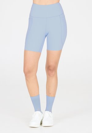 Helle blaue High-Waist-Radshorts aus dehnbarem Stoff mit Seitennähten. Kombiniert mit hellblauen Socken und weißen Turnschuhen.