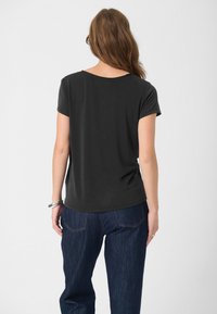 Černé tričko s krátkým rukávem a kulatým výstřihem, vyrobené z měkkého materiálu a uvolněného střihu, spárované s tmavě modrými džíny s jemným švem.