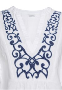 Weiße Bluse mit tiefem V-Ausschnitt und aufwändiger marineblauer Blumenstickerei entlang des Ausschnitts. Der Stoff wirkt leicht und strukturiert.