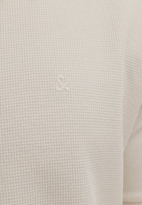 Gros plan d’un tissu blanc texturé avec un petit symbole esperluette brodé centré sur la surface.