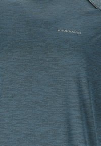 Blå atletisk polo skjorta gjord av strukturerad tyg, med ett subtilt randmönster och ordet "ENDURANCE" i silver på bröstet.