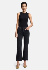 Schwarzes, geripptes, ärmelloses Oberteil, kombiniert mit hoch taillierten schwarzen Jeans mit fransigem Saum. Modell trägt gemusterte High Heels.