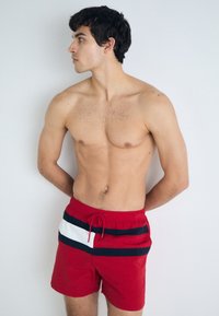 Rote Schwimmshorts mit elastischem Bund und Kordelzug, die an der Vorderseite navyblau-weiße horizontale Streifen aufweisen.