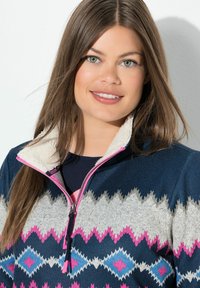 Marineblaues Fleece-Jackett mit einem pinken und grauen geometrischen Muster, das über einen Reißverschlusskragen mit Fleece-Futter und kontrastierenden Akzentfarben verfügt.