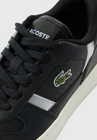 Sneaker in pelle nera con superficie testurizzata, striscia bianca a contrasto e logo di coccodrillo verde ricamato. Presenta lacci neri e linguetta imbottita.