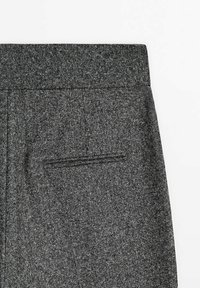 Gros plan sur l'arrière d'un pantalon en laine gris foncé montrant une ceinture et une poche passepoilée unique.